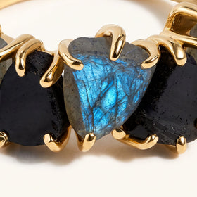 Yellow gold-tone claws frame the blue surface of a raw labradorite and the dark stones beside it.