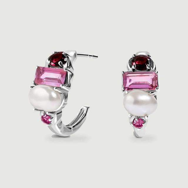 Two silver-tone hoops display deep red garnet, rectangular pink stones and white pearls on a pale gray surface.