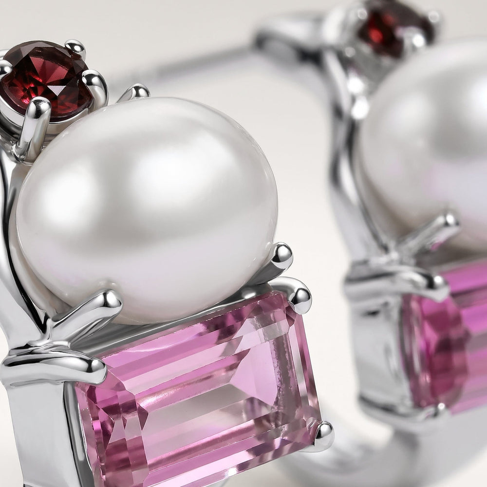 A close view shows the white pearl, red garnet and faceted pink stone held by polished silver-tone prongs.