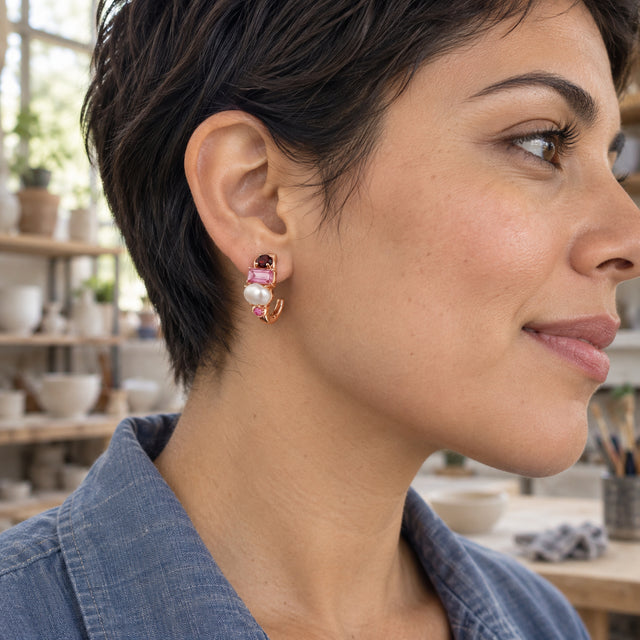 A woman with a dark pixie haircut wears a rose gold-tone gemstone and pearl hoop in a ceramics studio.
