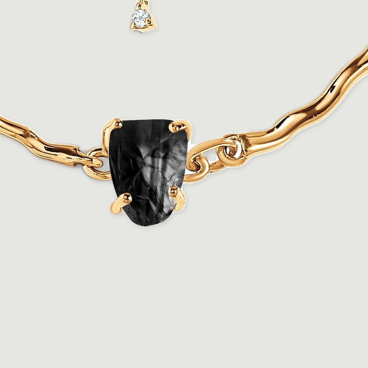 A close view shows the rough black stone held by yellow gold prongs between sculpted links.