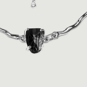 Silver prongs secure an irregular black stone beside polished curved chain links in close detail.