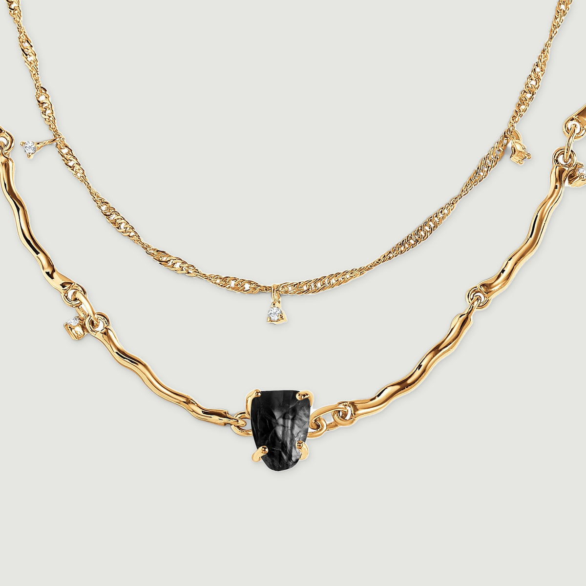 The lower arcs of two yellow gold chains surround a black stone, with small clear charms on the finer chain.