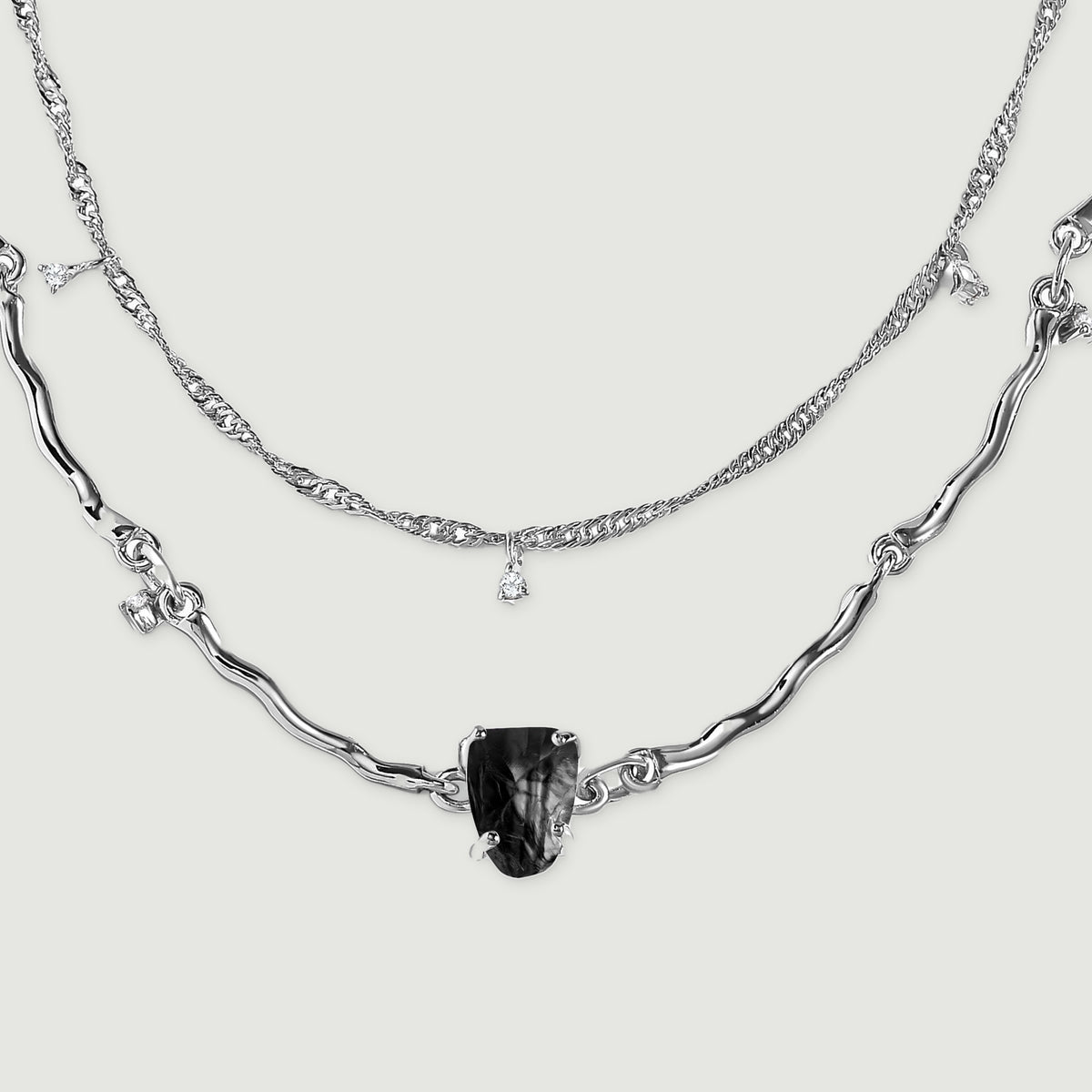 Two silver chain arcs lie flat, showing textured fine links above a sculpted strand with a black center stone.