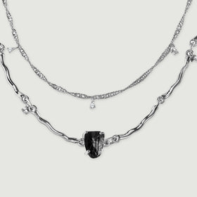 Two silver chain arcs lie flat, showing textured fine links above a sculpted strand with a black center stone.