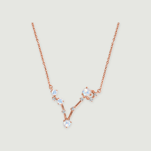The rose gold vermeil necklace has a V-shaped arrangement of four round moonstones and small clear accents on a light gray background.