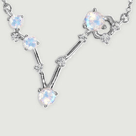 Four round moonstones and small clear accents form a silver V-shaped pendant between two sections of fine chain.