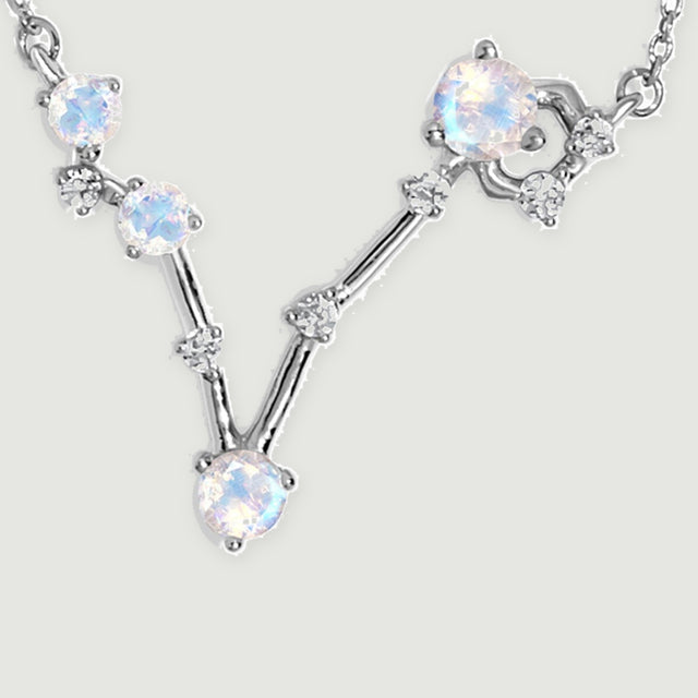 Four round moonstones and small clear accents form a silver V-shaped pendant between two sections of fine chain.