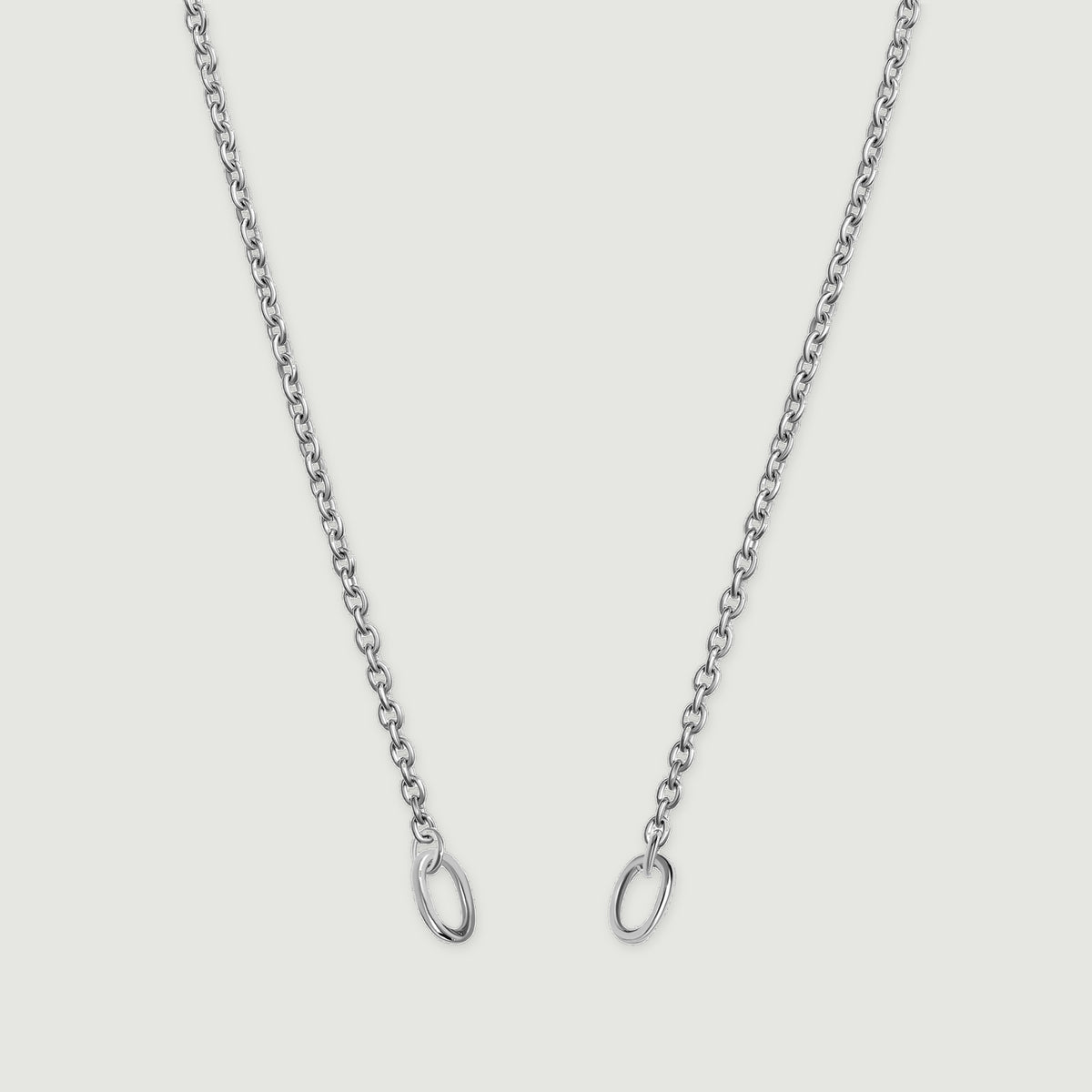 A fine silver chain descends in two strands with an oval ring at each end against a light gray background.