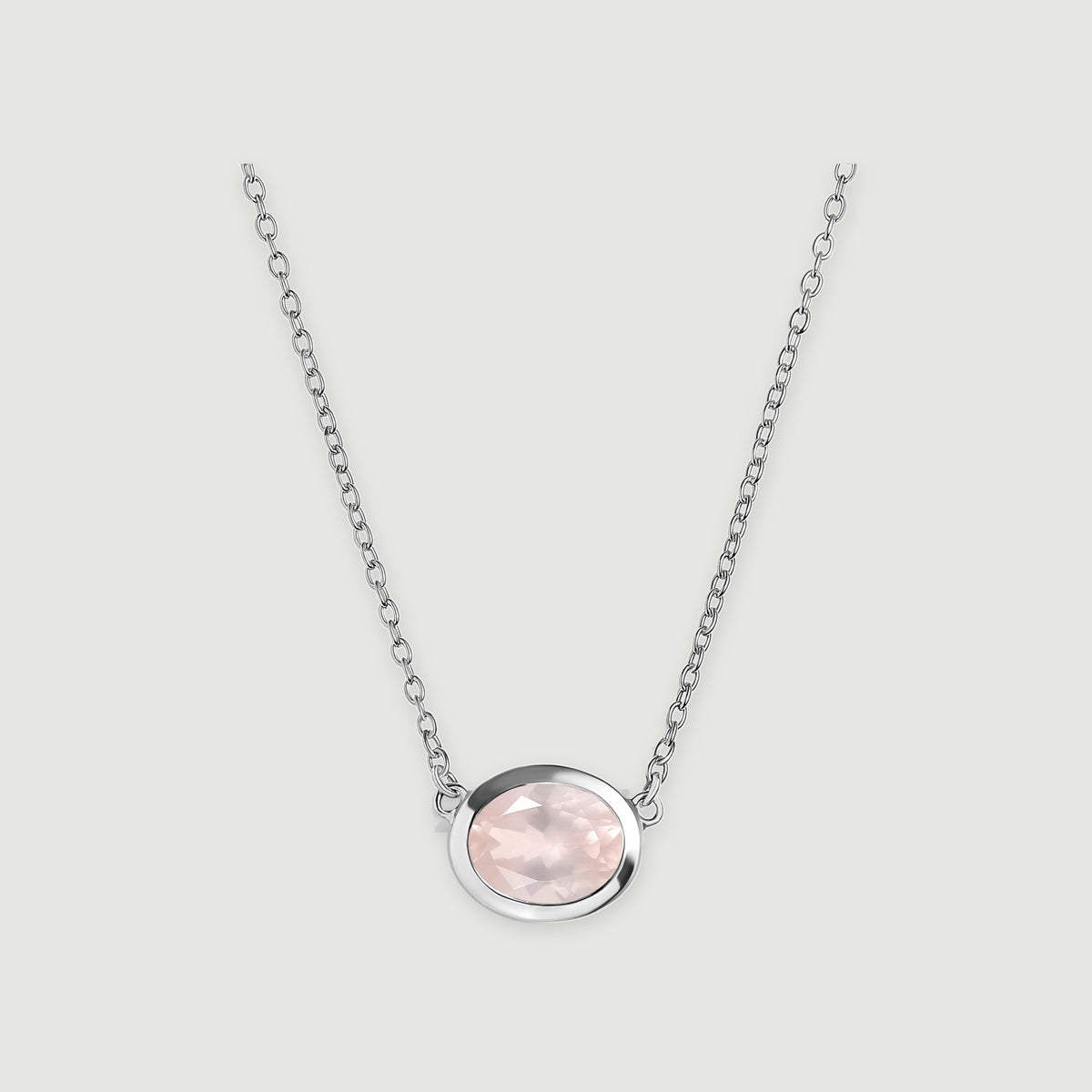 A pale pink oval rose quartz pendant sits in a polished white metal bezel on a fine link chain against a light gray background.