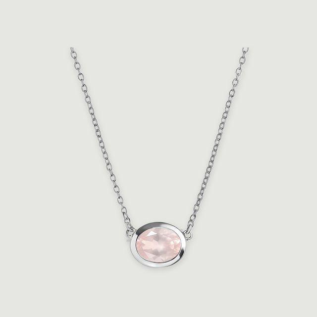 A pale pink oval rose quartz pendant sits in a polished white metal bezel on a fine link chain against a light gray background.