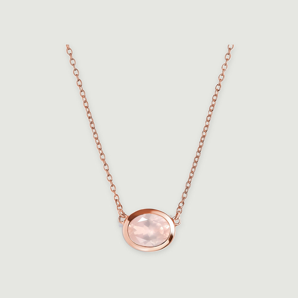 A rose gold colored chain joins the sides of a faceted pink oval pendant centered on a light gray surface.