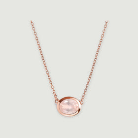 A rose gold colored chain joins the sides of a faceted pink oval pendant centered on a light gray surface.