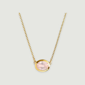 A yellow gold colored bezel surrounds a pale pink oval stone beneath two lengths of matching link chain on light gray.