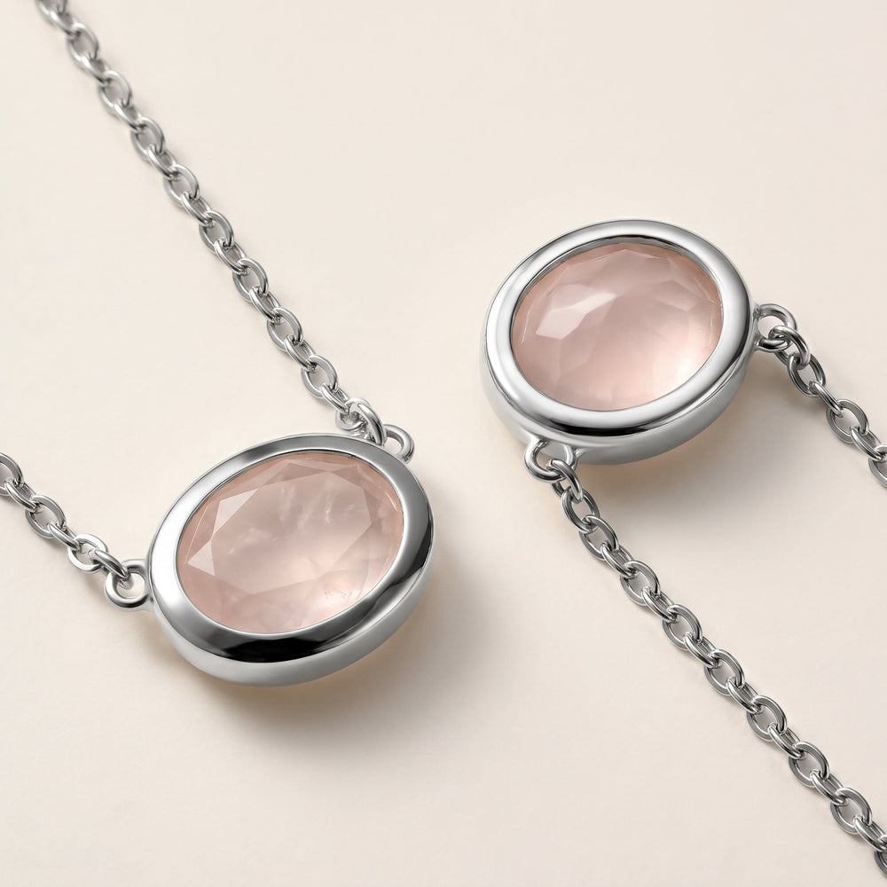Two close views show the pale pink stone facets, white metal bezel edges, and small connecting chain links on a cream tabletop.