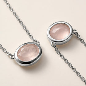 Two close views show the pale pink stone facets, white metal bezel edges, and small connecting chain links on a cream tabletop.