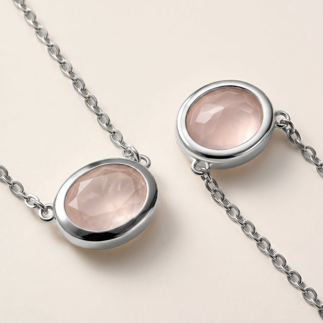 Two close views show the pale pink stone facets, white metal bezel edges, and small connecting chain links on a cream tabletop.