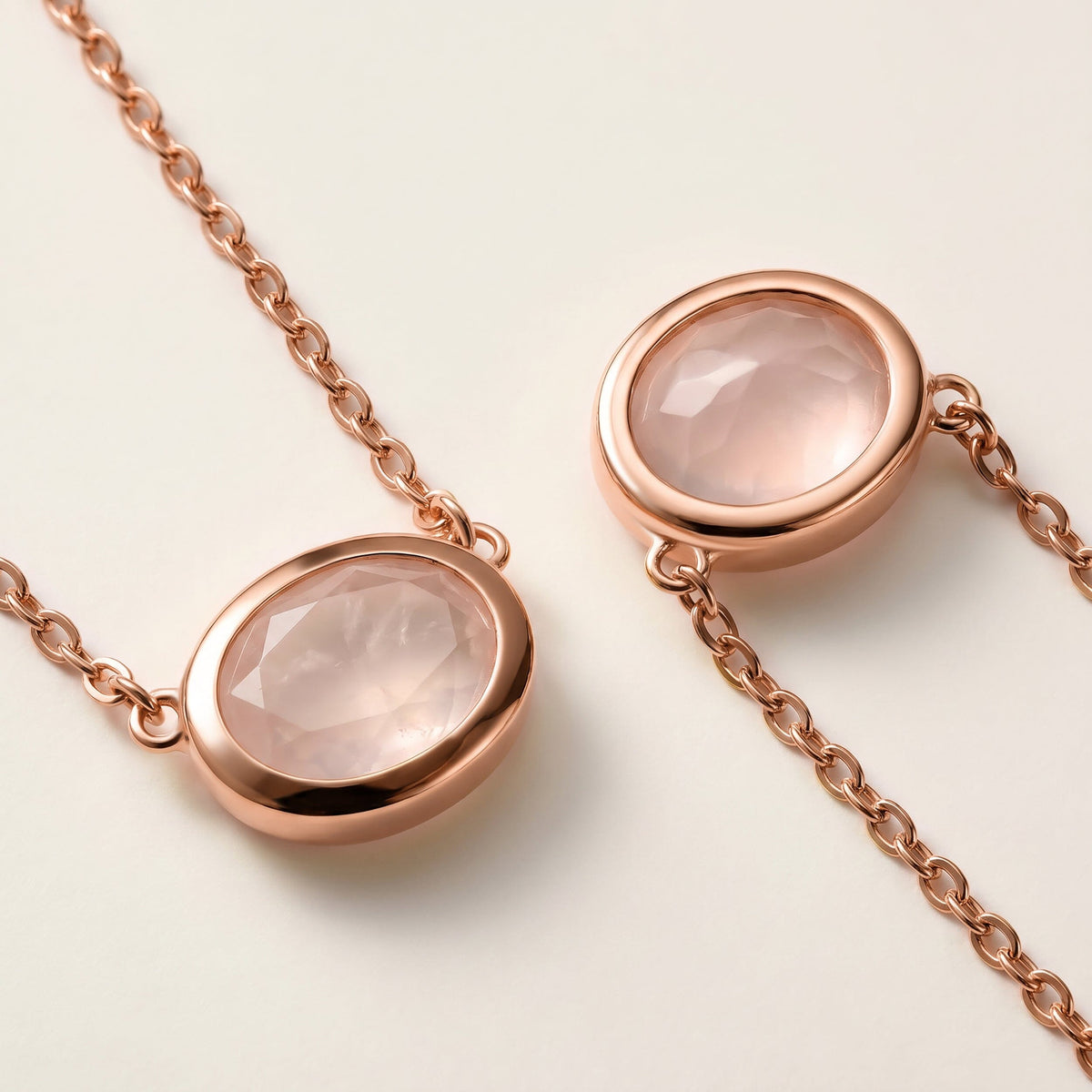 Rose gold colored oval bezels and fine chain connections frame two faceted pink stones in a close view on a cream surface.