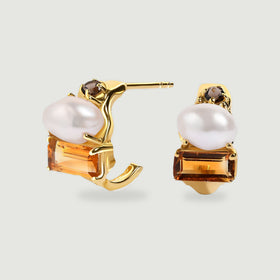 A pair of yellow gold open hoop earrings displays white pearls, rectangular amber-colored citrine and small round brown stones on a light gray surface.