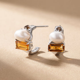 Silver-tone earrings stand on a pale textured surface with their posts visible behind the pearl and citrine settings.