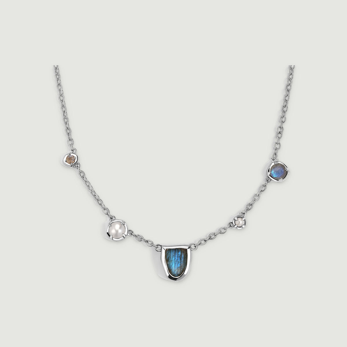 A silver-tone necklace has a blue labradorite centerpiece, two pearls, and two round stones on a light gray background.