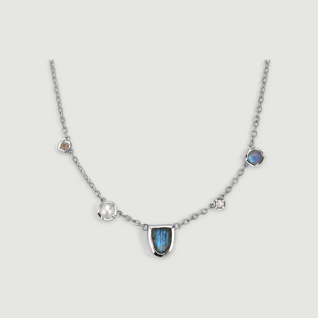 A silver-tone necklace has a blue labradorite centerpiece, two pearls, and two round stones on a light gray background.