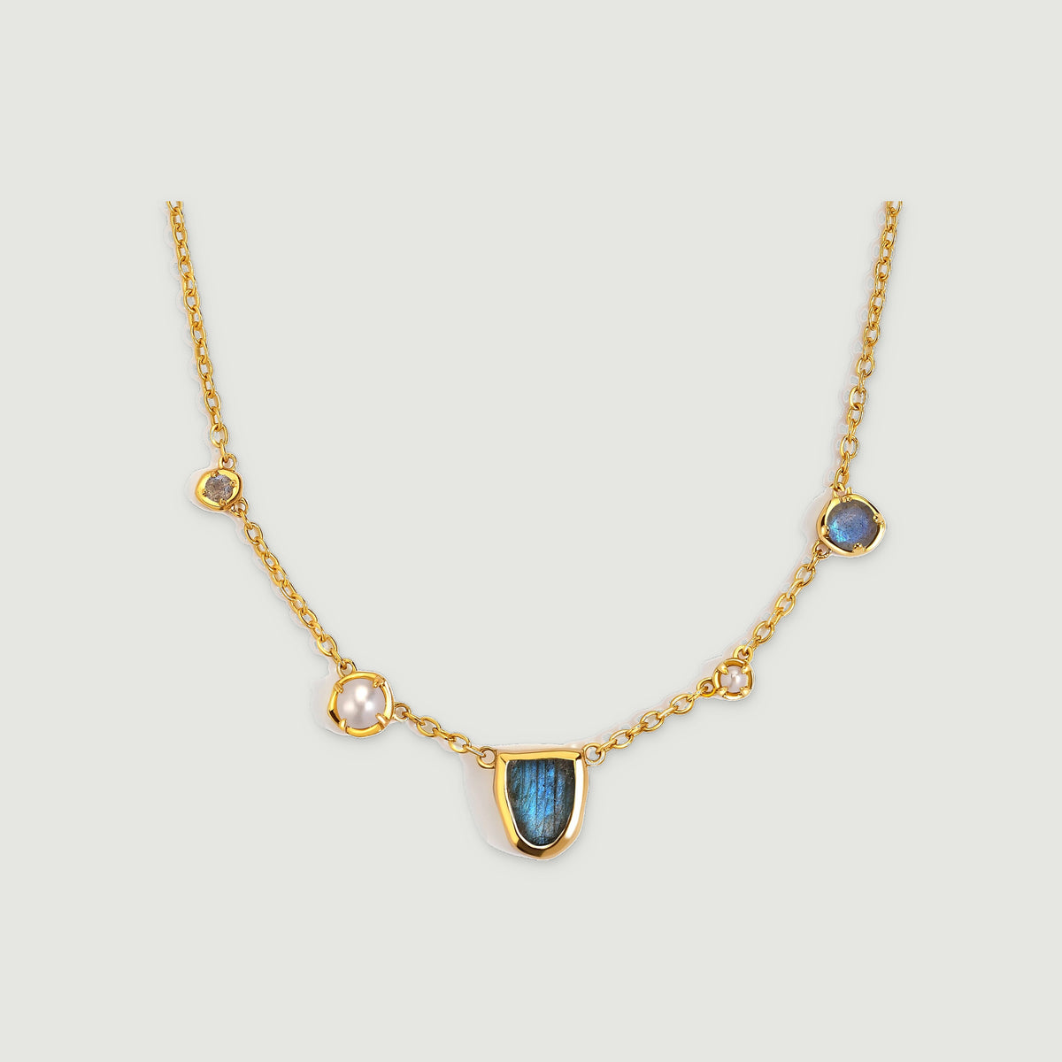 A yellow gold-tone chain connects a shield-shaped labradorite center with round pearl and stone stations.