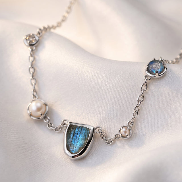The silver-tone labradorite and pearl necklace rests across folds of pale fabric.