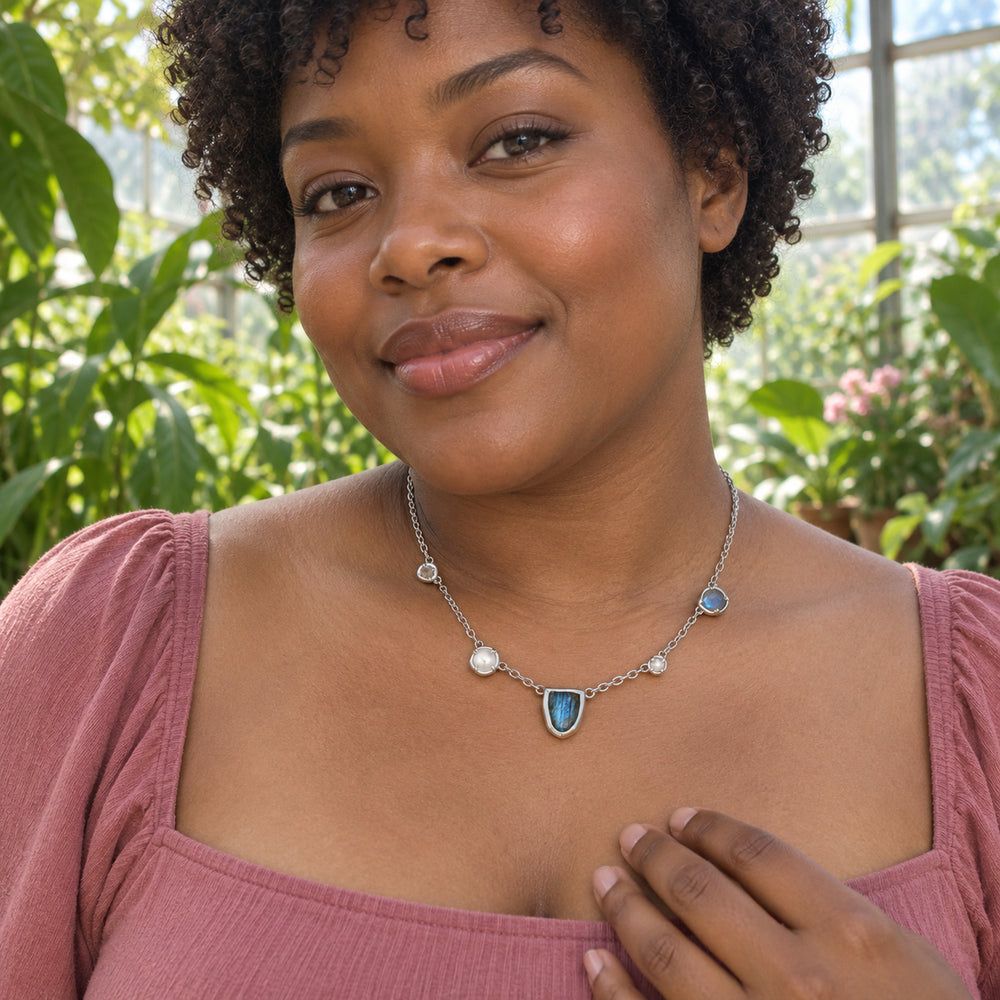 A woman in a rose square-neck top wears the silver-tone labradorite and pearl necklace in a leafy greenhouse.