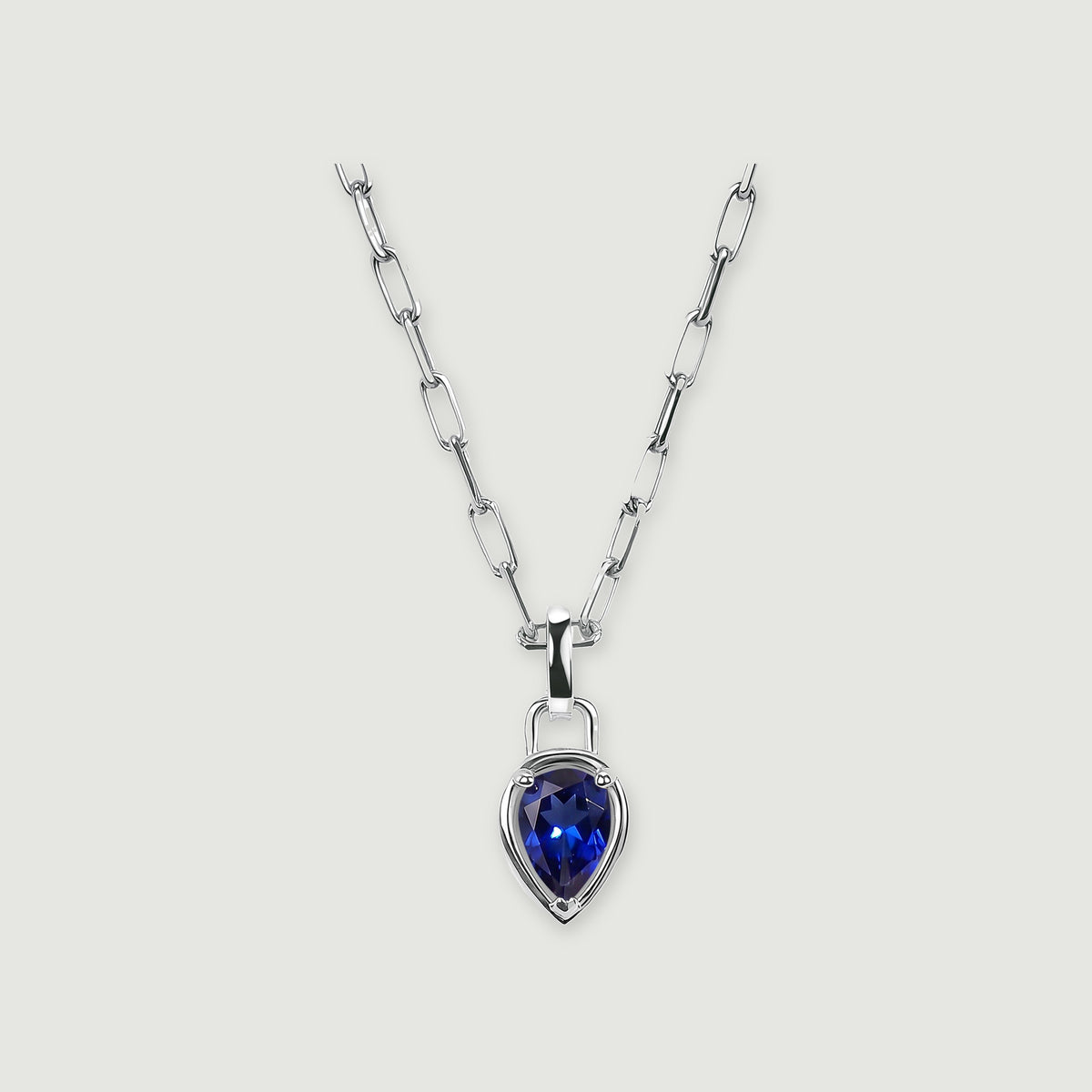 A pear-shaped deep-blue pendant hangs from a polished silver-tone rectangular-link chain on a light gray background.