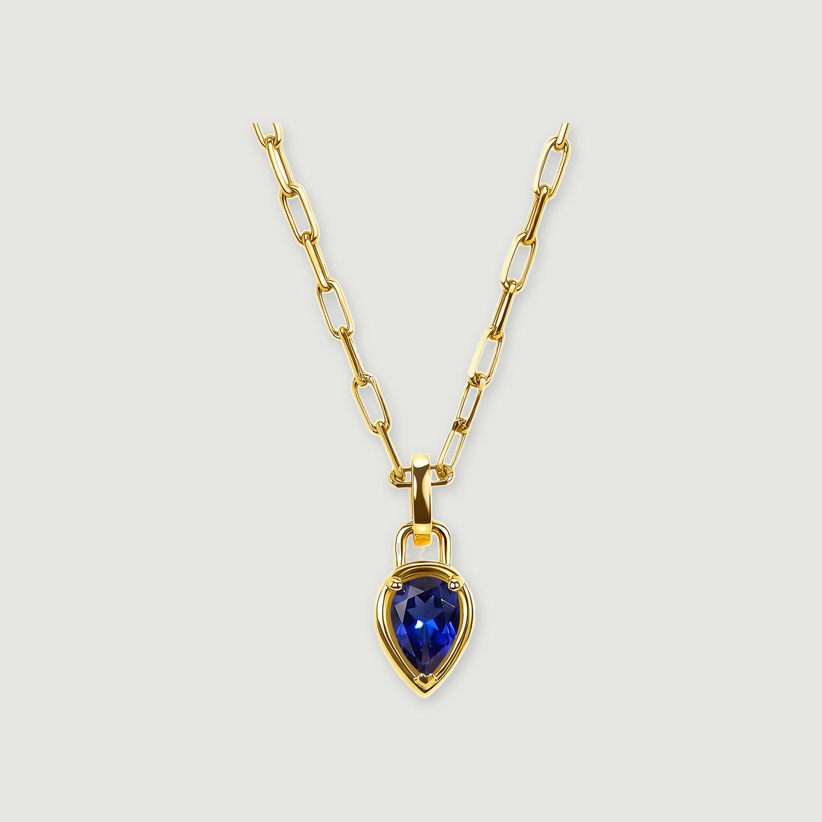 A pear-shaped deep-blue pendant hangs from a polished yellow-gold-tone rectangular-link chain on a light gray background.