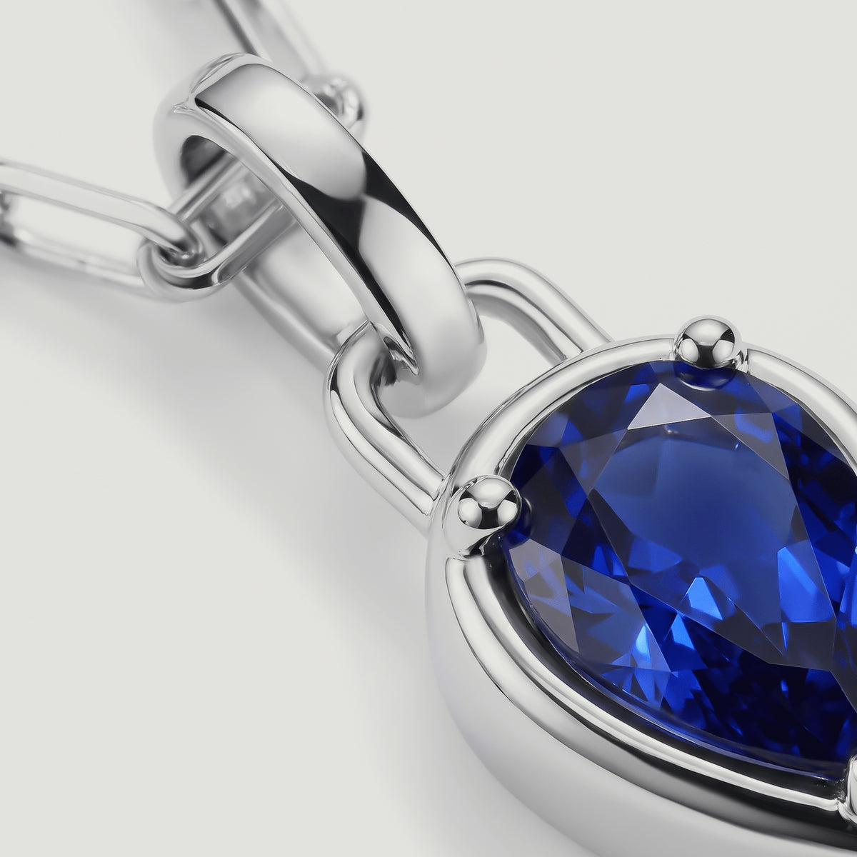 A close-up shows the blue gemstone facets, silver-tone prongs, and polished pendant bail.