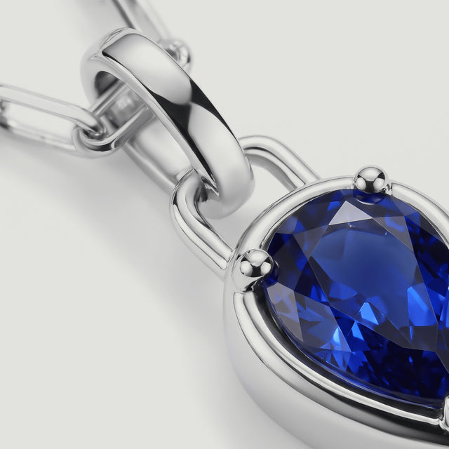 A close-up shows the blue gemstone facets, silver-tone prongs, and polished pendant bail.