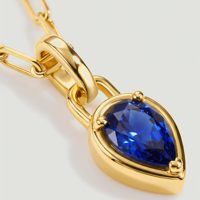 The deep-blue pear-shaped stone sits inside a yellow-gold-tone rim beneath a smooth pendant bail.