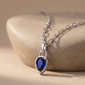 The silver-tone blue pendant rests against a rounded beige stone with the rectangular chain links visible above it.