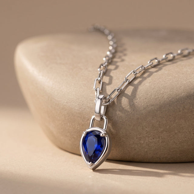 The silver-tone blue pendant rests against a rounded beige stone with the rectangular chain links visible above it.