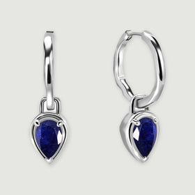 A pair of silver-tone hoops with deep blue pear-shaped sapphire drops rests on a light gray surface.