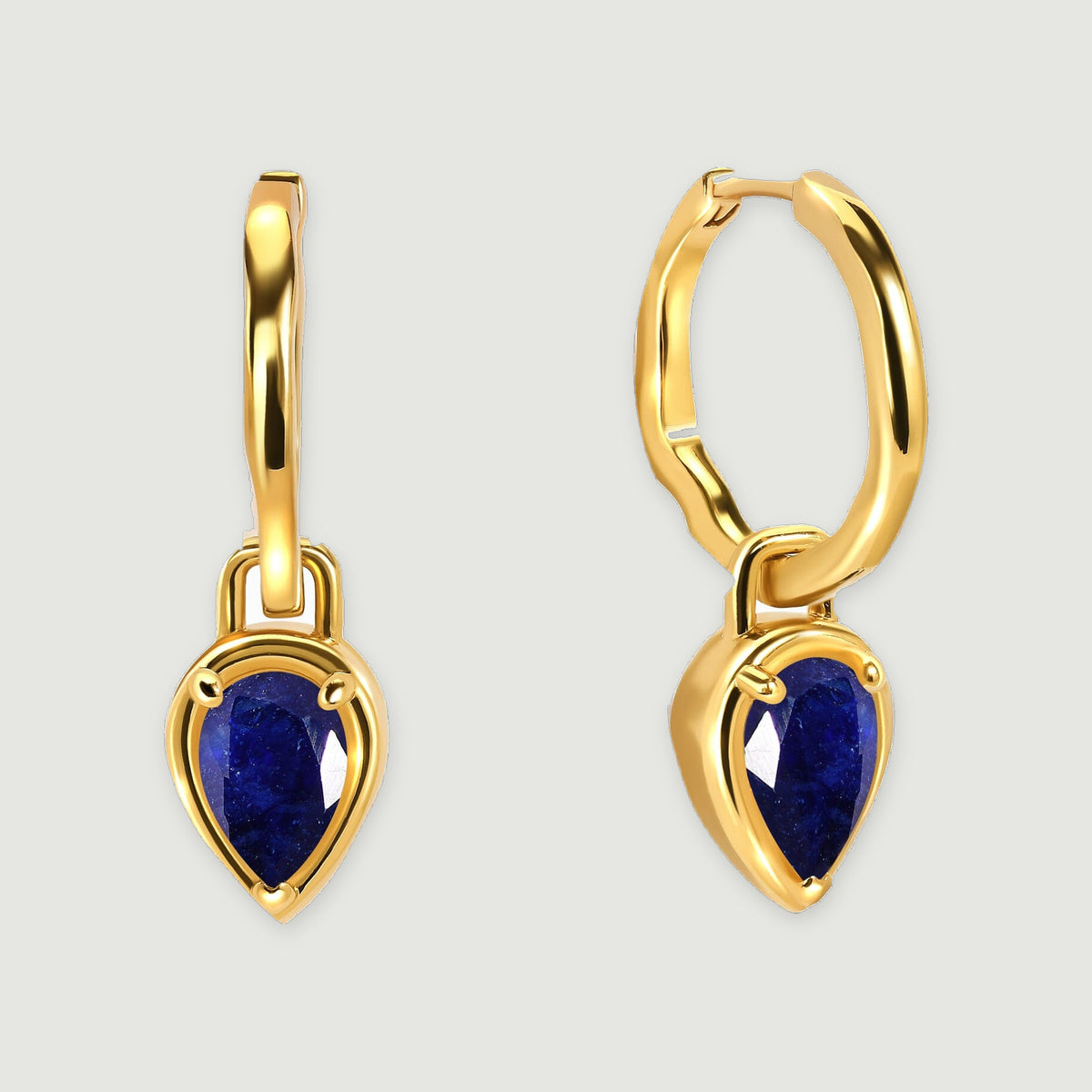 Two yellow gold-tone hoop earrings with blue sapphire drops stand side by side on a pale gray background.