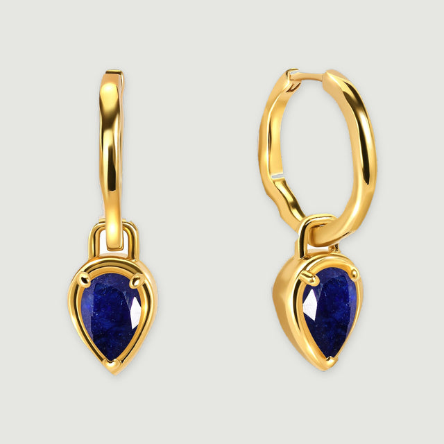 Two yellow gold-tone hoop earrings with blue sapphire drops stand side by side on a pale gray background.