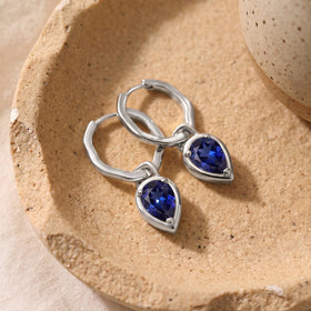 Silver-tone sapphire hoops lie together on a textured beige stone tray.