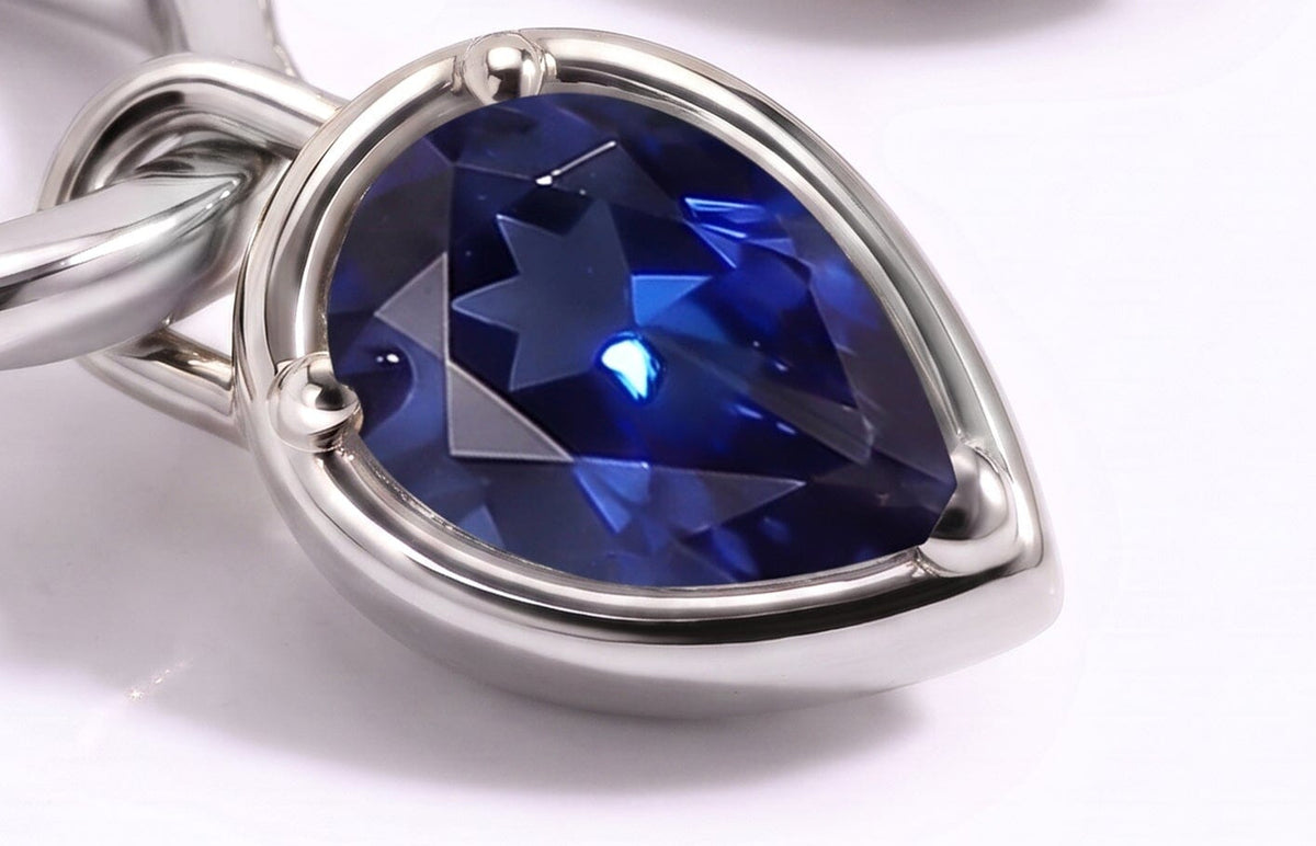 A close view shows the facets and three rounded prongs of a blue pear-shaped sapphire in a silver-tone setting.