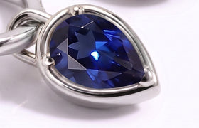 A close view shows the facets and three rounded prongs of a blue pear-shaped sapphire in a silver-tone setting.