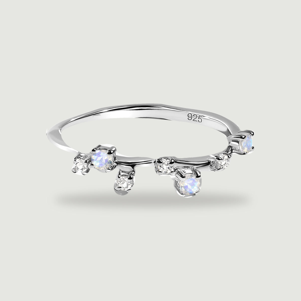 A sterling silver ring with staggered round moonstones and clear stones rests on a light gray surface.