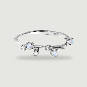 A sterling silver ring with staggered round moonstones and clear stones rests on a light gray surface.