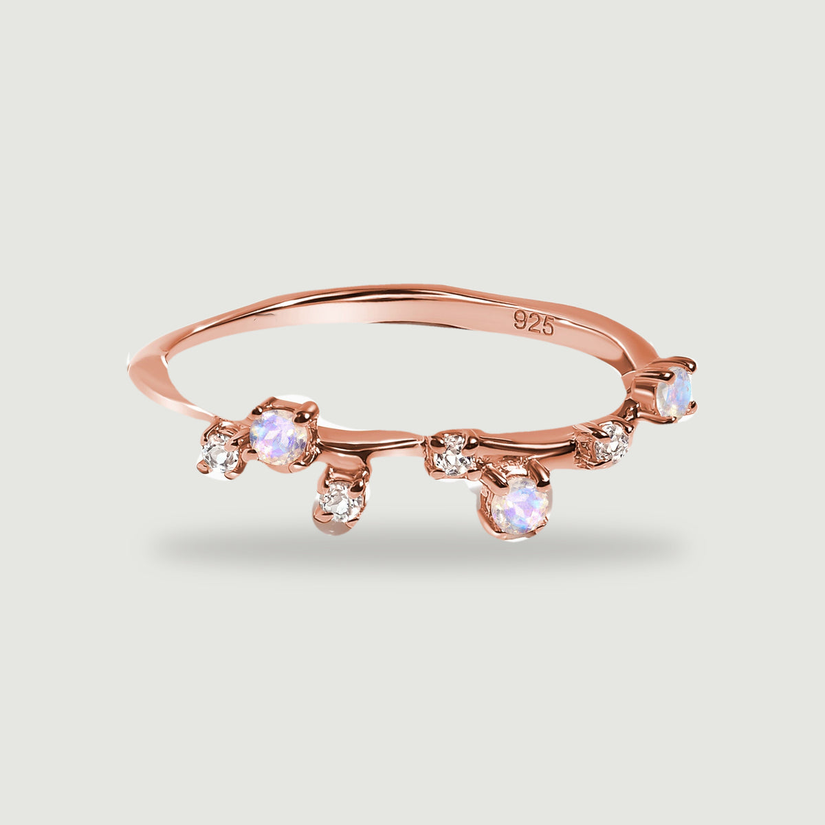 A rose gold vermeil ring with offset moonstones and clear accents casts a soft shadow on light gray.