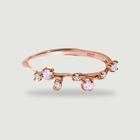 A rose gold vermeil ring with offset moonstones and clear accents casts a soft shadow on light gray.