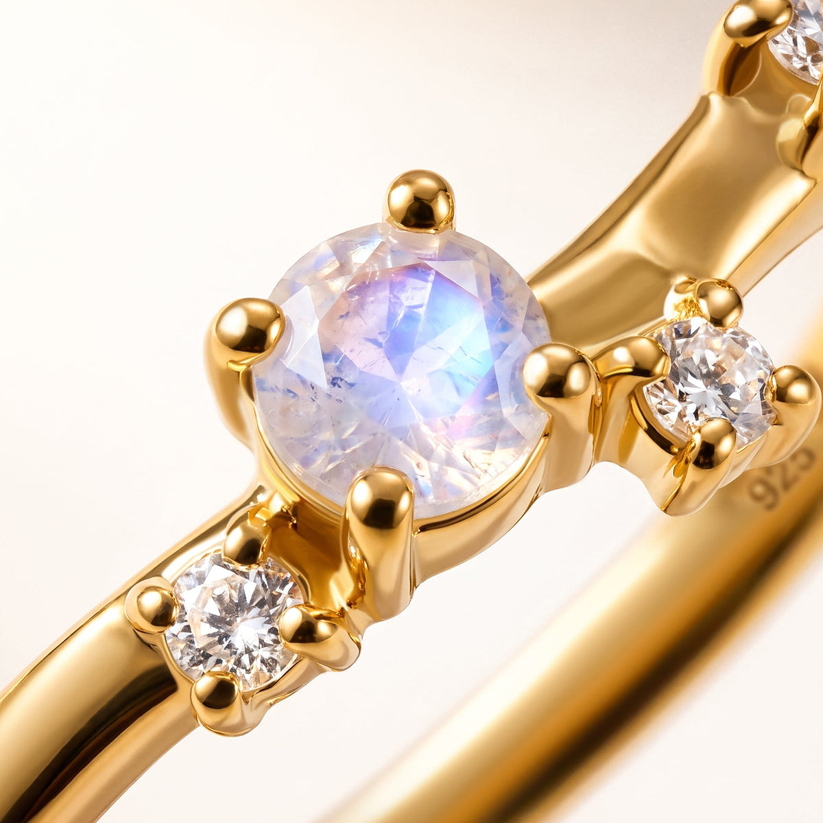 A faceted moonstone and two clear round stones are shown close up in yellow gold vermeil prong settings.