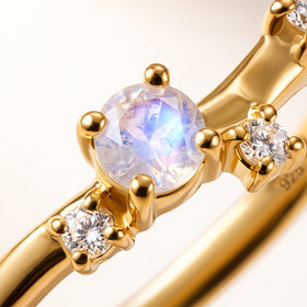 A faceted moonstone and two clear round stones are shown close up in yellow gold vermeil prong settings.