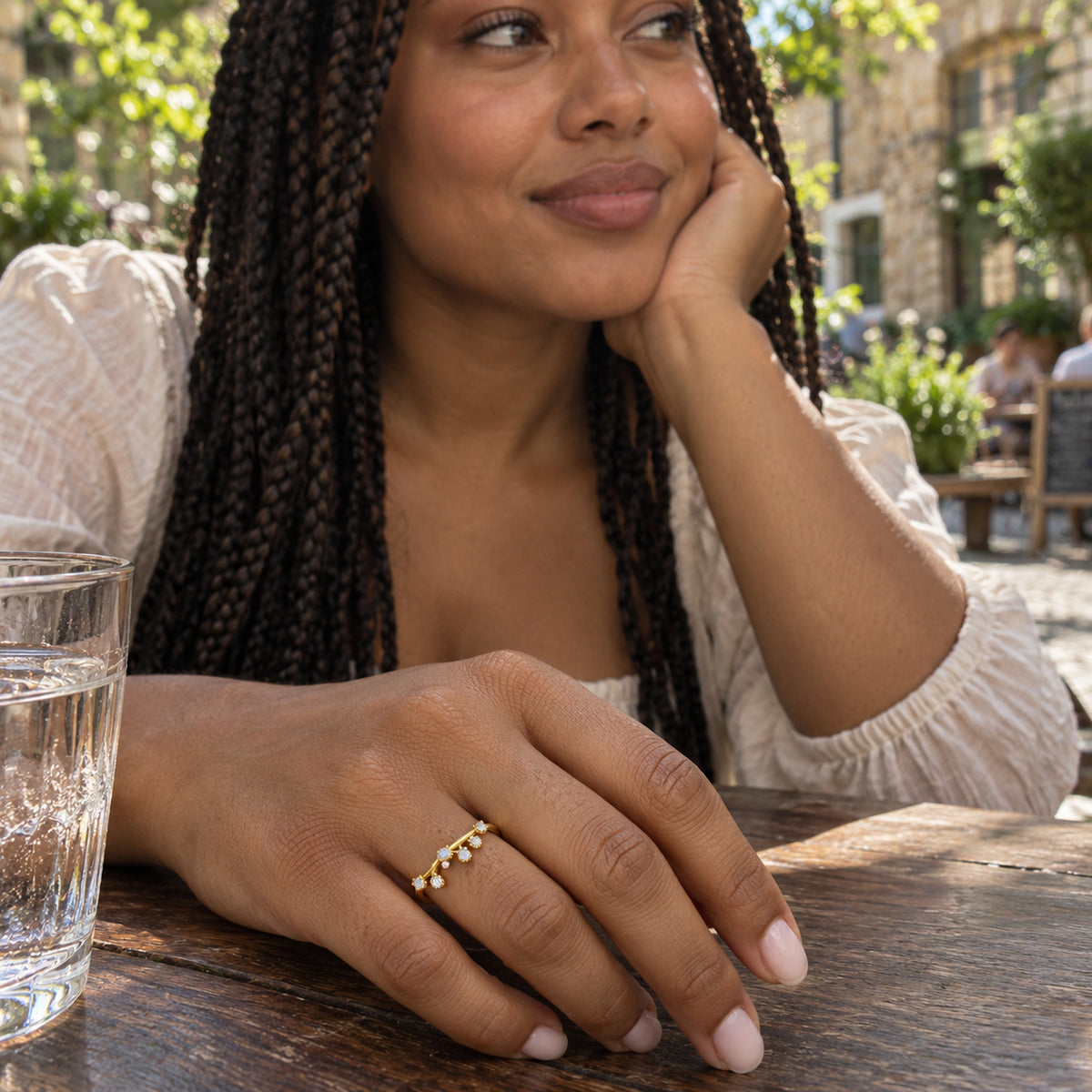 A yellow gold vermeil moonstone band is shown on a hand resting on a wooden table at an outdoor cafe.