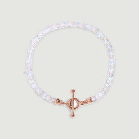 A circle of faceted moonstone beads ends in a rose gold bar and round clasp on a pale gray surface.